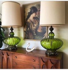 two green glass lamps sitting on top of a wooden dresser next to a lamp shade