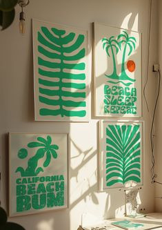 three green and white art prints hanging on the wall next to a desk with a lamp