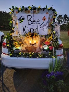 the back end of a white car decorated with flowers and bees is shown in front of a sign that says bee kind