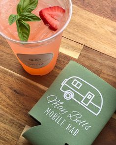 a drink in a glass next to a book on a wooden table with a green cover