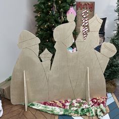 a wooden cutout of three people in front of a christmas tree with presents on the floor