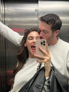 a man and woman taking a selfie in front of an elevator door with their cell phone