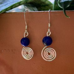 These earrings are made of round  Lapis Lazuli stones that sit atop decorative hand wrapped sterling silver wire spirals. Measuring one and a quarter (1.25) inches long, these earrings are a nice addition to any outfit. The sterling silver ear hooks on these earrings are perfect for even the most sensitive ears. These earrings make a great gift and gift wrapping comes standard with any purchase. A little bit about the gemstone used in this piece: Lapis Lazuli encourages self-awareness, allows se Nickel-free Spiral Blue Earrings, Handmade Round Lapis Lazuli Earrings, Lapis Jewelry, Lapis Earrings, Marble Earrings, Wrapped Earrings, Healing Crystal Jewelry, Sterling Silver Wire Wrap, Chakra Jewelry