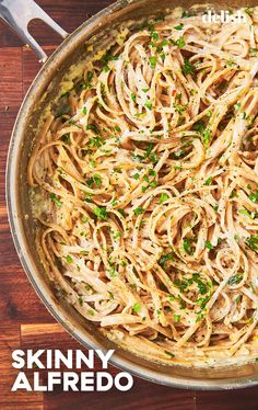 a pan filled with pasta and parsley on top of a wooden table