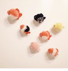 six small stuffed animals are arranged in a row on a white surface, one is black and the other is orange