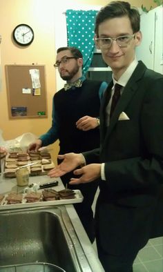 two men in suits and ties are standing near a kitchen sink with food on the counter