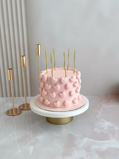 a pink cake sitting on top of a white plate next to two gold candles and a candle holder