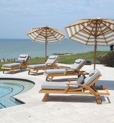 lounge chairs and umbrellas next to a swimming pool with the ocean in the background