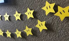 some yellow paper stars are hanging on a string in front of a gray carpeted wall