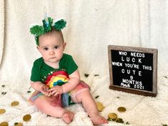 a baby sitting next to a sign that says who needs luck when you're this cute month