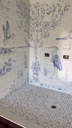 a bathroom with blue and white wallpaper, tile flooring and a bird mural on the shower