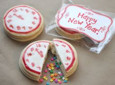 two decorated cookies with white frosting and sprinkles in front of a happy new year sign