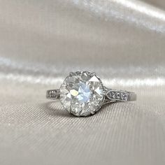 an old cut diamond ring sits on a shiny surface with white fabric in the background