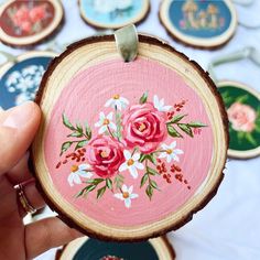 a hand holding a piece of wood with pink flowers painted on it and other wooden slices