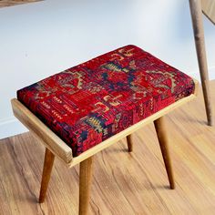 a small wooden bench with a red and blue patterned seat cover on it's legs