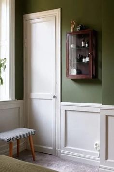 a room with green walls and white paneling on the wall, along with a small bench