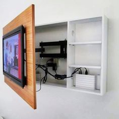 a tv mounted to the side of a wall next to a shelf with wires on it