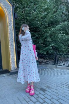 a woman standing in front of a building wearing pink shoes and a white dress with red polka dots