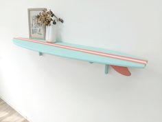 a blue surfboard mounted to the side of a wall next to a vase with flowers