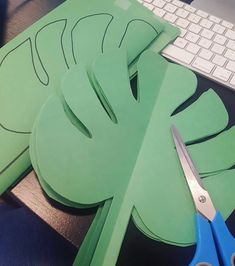 green paper cutouts sitting on top of a desk next to a keyboard and scissors