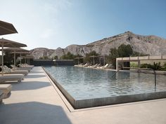 an empty swimming pool surrounded by lounge chairs and umbrellas with mountains in the background