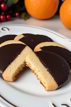 chocolate covered cookies on a white plate with oranges in the backgroung