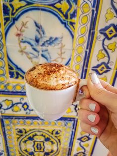 a woman holding a cup of coffee in front of a colorful wall with blue and yellow tiles