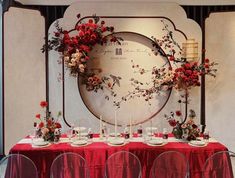 a red table topped with lots of plates and chairs next to a wall mounted clock