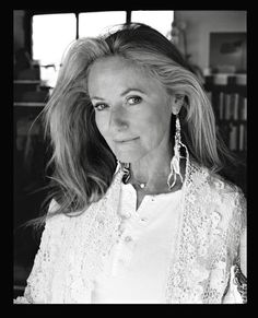 a black and white photo of a woman with long blonde hair wearing earrings, looking at the camera