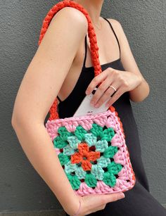 a woman is holding a crocheted bag with an orange and green flower on it