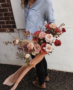 a woman holding a bouquet of flowers in front of a brick wall with her hands on the ground