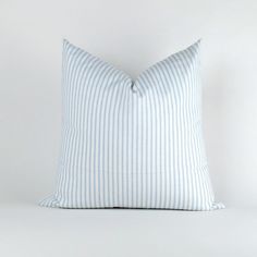 a blue and white striped pillow sitting on top of a white bedding set in front of a white wall