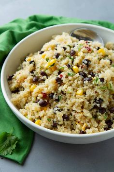 a white bowl filled with rice and beans on top of a green napkin next to a spoon