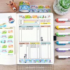 an open planner with stickers and pens next to it on a wooden table top