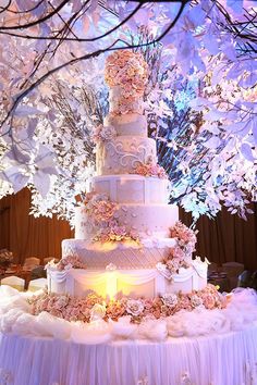 a large wedding cake sitting on top of a table under a tree with pink flowers