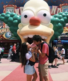 a man and woman standing next to each other in front of a large cartoon character