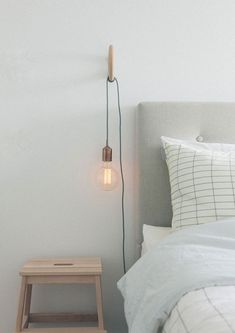 a light that is on the side of a bed next to a night stand and stool