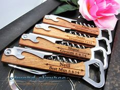 four bottle openers with engraved names on them and a pink rose in the background