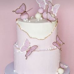 a three tiered cake with pink butterflies and pearls on the top, sitting on a table