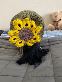 a crocheted sunflower hat on top of a bed next to a teddy bear