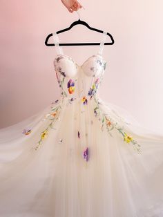 a white dress with flowers on it hanging from a hanger in front of a pink wall