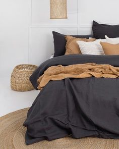 the bed is made with black linens and brown pillows, along with a wicker basket