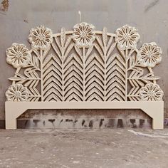 an intricately carved wooden headboard with flowers and leaves on the top, against a gray wall