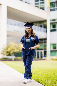 a woman in graduation cap and blue scrubs standing on the sidewalk outside an office building