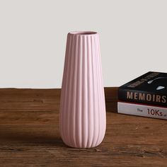 a pink vase sitting on top of a wooden table next to a stack of books