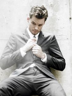 a man in a suit and tie sitting on the ground with his hands under his chin