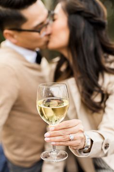 a man and woman kissing while holding a wine glass with white wine in front of them