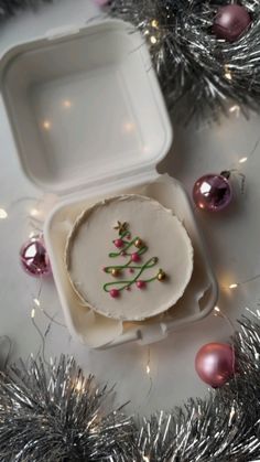 a small white box with some ornaments in it and a christmas tree decoration on the lid