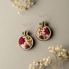 two earrings with flowers on them sitting next to some white flowers and one is pink