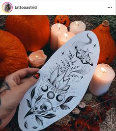 a person holding a paper board with tattoos on it next to candles and pumpkins